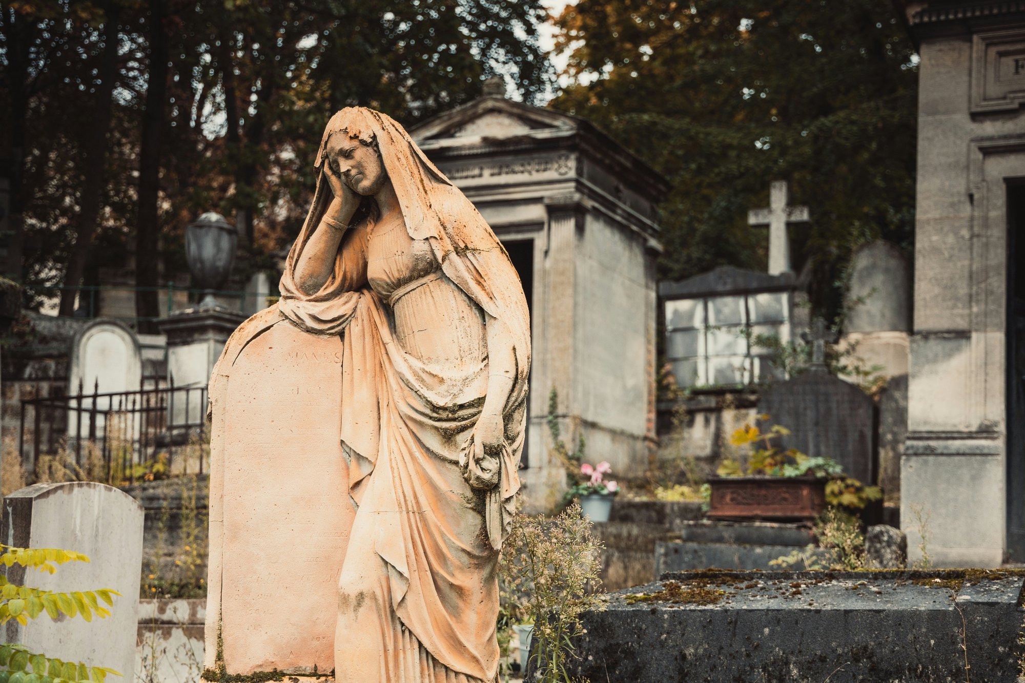 A stone figure leans over a grave stone in Pere Lachaise cemetary, Paris France